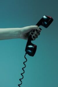Moody close-up of a hand holding a vintage telephone receiver against a blue background.